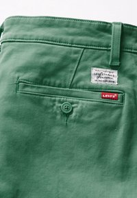 Gröna denimbyxor med en bakficka med knappar, Levi Strauss-märke och röd Levi's etikett. Slät textur, klassisk design, synlig sömnad.