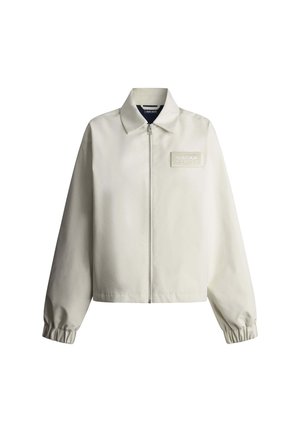 Béžová bunda na zips s elastickými manžetami, špicatým golierom a malým obdĺžnikovým logo nášivkou na ľavej strane hrudníka.