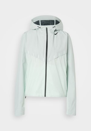 Ανοιχτό πράσινο αδιάβροχο μπουφάν Nike με κουκούλα, μαύρο φερμουάρ και μαύρο λογότυπο Nike στο πάνω αριστερό μέρος του στήθους.