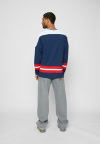 Cămașă navy cu mânecă lungă, având dungi roșii și albe la tiv. Asortată cu pantaloni gri deschis, care oferă un aspect lejer și un stil casual.