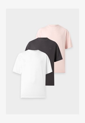 Deux personnes se tiennent devant un fond blanc, portant des hauts rose clair et un jean bleu, l'une tient un grand sac à épaule sombre.