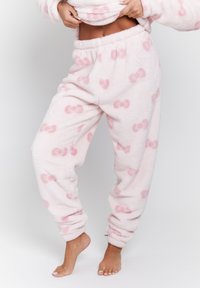 Ljust rosa, plyschiga pajamasbyxor med en mjuk textur, med ett upprepat rosett-mönster. De har en elastisk midja och smalnande anklar.