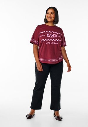 Burgundy graphic t-shirt with "LIVE STREAM" text, short sleeves and checkered pattern; paired with black straight-leg pants and glossy shoes.