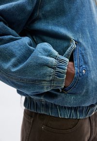 Džínsová bunda s voľným strihom, svetlomodrej farby, s rebrovanými manžetami a elastickým pásom. Má bočné vrecká a viditeľný gombík ako dekoráciu.