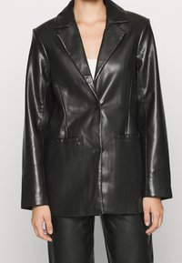 Czarna skórzana marynarka z klapą z wycięciem, pojedynczym zapięciem na guzik oraz dwoma przednimi kieszeniami, o gładkiej, błyszczącej fakturze.