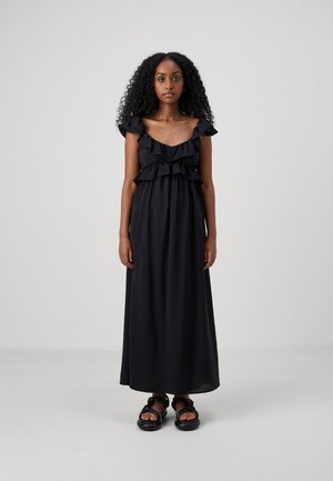 Svart maxikjole med volanger på skulderstroppene og lagdelt overdelen. Glatt stoff med en avslappet passform, kombinert med kraftige svarte sandaler. Bred hemline.
