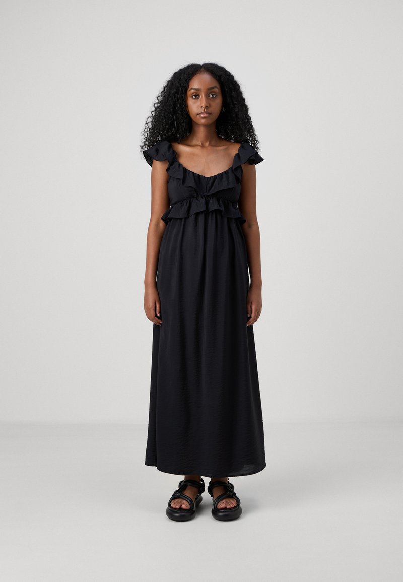 Μαύρο μέγιστο φόρεμα με ριγέ τιράντες και στρωτό μπούστο. Λείο ύφασμα με χαλαρή εφαρμογή, συνδυασμένο με χοντρές μαύρες σανδάλες. Εκτενής πλαϊνή ραφή.