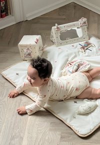 Miękka bawełniana mata do zabawy w stonowanych kolorach z wzorem gwiazdek, trzy pluszowe klocki z wzorami karnawałowymi oraz lusterko, które wzbogacają sensoryczną zabawę.