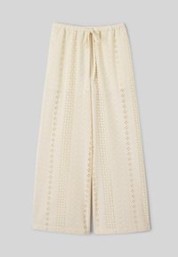 Pantalon large crème en tissu ajouré, taille élastique et lien à nouer sur le devant, posé à plat sur un fond gris clair.