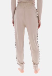Beige joggingbukser med en tekstureret sidepanel, elastisk talje og tilspidsede ben. Glat stof med en diskret glans.