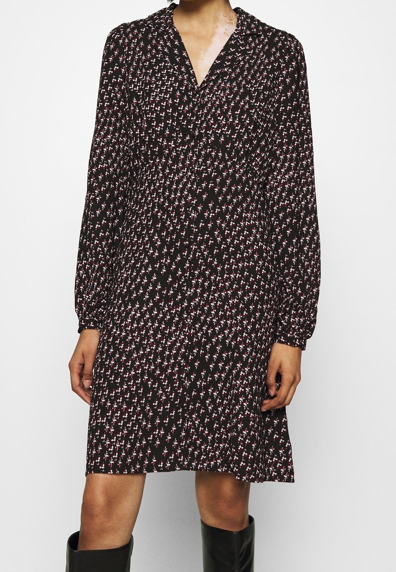 Femme portant une robe noire à manches longues avec de petits motifs floraux roses et blancs, et des bottes noires montantes jusqu'aux genoux.