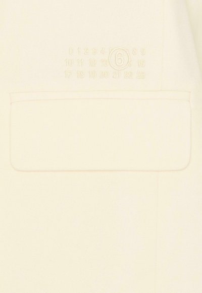 Tekstylia kremowego koloru o teksturowanym wykończeniu z kieszenią ozdobioną tłoczonymi cyframi i okrągłym akcentem. Delikatne różowe przeszycia.