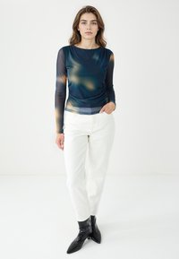 Top a maniche lunghe, leggero, di colore blu scuro con un motivo sfumato; abbinato a pantaloni bianchi e stivali alla caviglia neri con punta affilata.