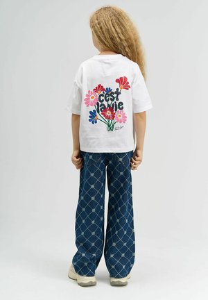 Hvid t-shirt med blomsterprint i rød, lyserød og blå på ryggen; parret med brede blå denimbukser med blomsterdesign og cremefarvede sneakers.