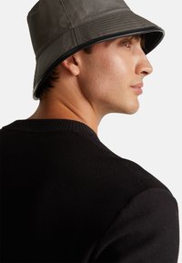 Cappello a secchiello grigio con finitura testurizzata e una ampia tesa, abbinato a un maglione nero a maglia con collo a girocollo classico.