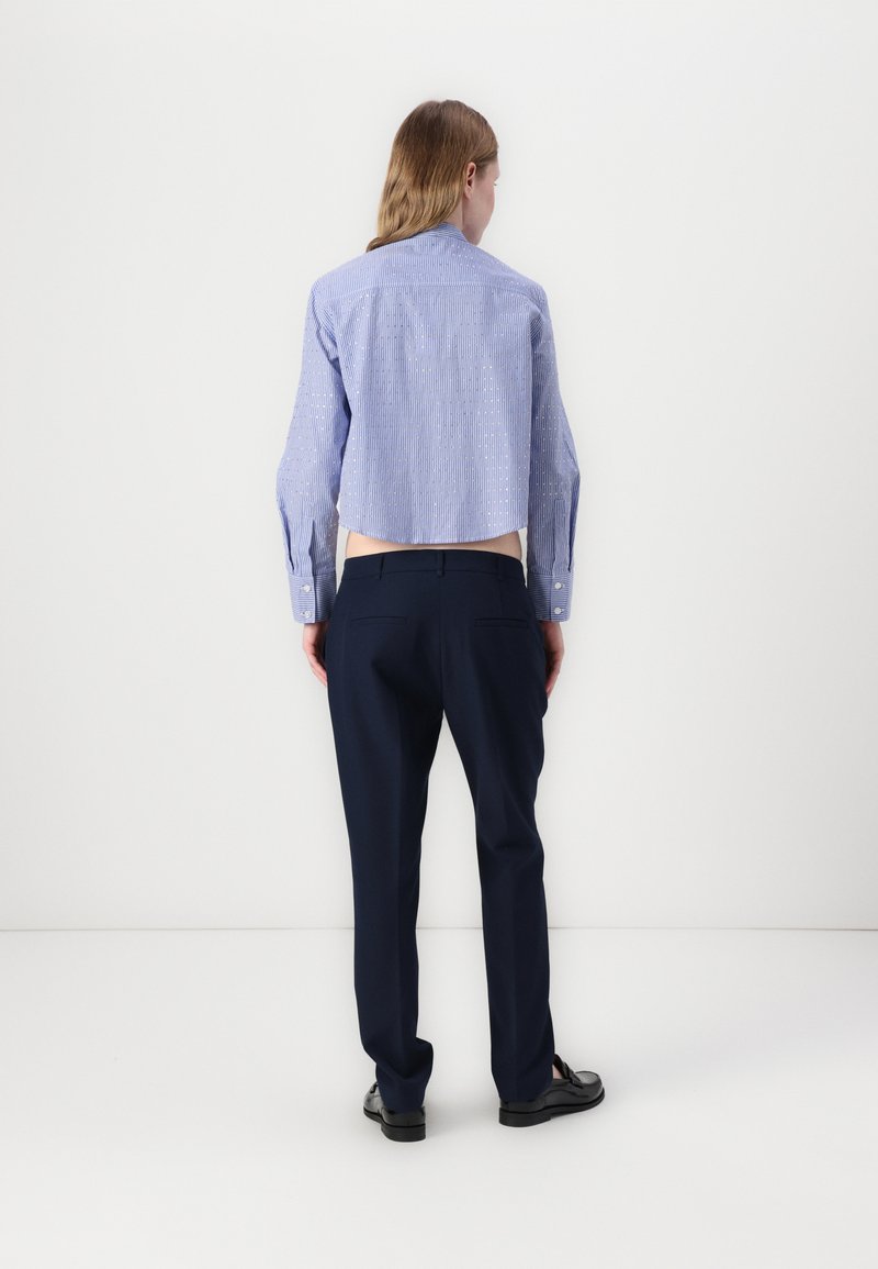 Camicia blu a righe con dettagli sui bottoni, abbinata a pantaloni blu scuro. L'outfit presenta una vestibilità su misura e trame di tessuti morbidi.