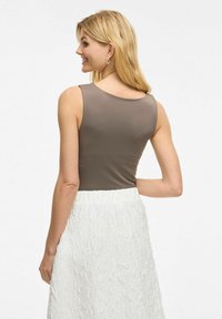 Brązowy bezrękawnik o gładkiej fakturze, w połączeniu z białą spódnicą o fakturze. Widok pokazuje tył stroju.