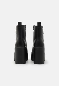 Stivali alla caviglia in pelle nera con tacco robusto, chiusura con zip e linguetta sul retro; texture liscia con dettagli di cucitura minimi.