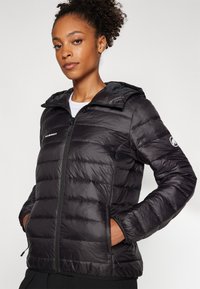 Zwarte pufferjack met een capuchon, voorzien van een gestikte textuur, een voorrits en een logo-accent op de mouw. Ontworpen voor warmte en comfort.
