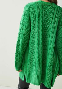 Grüner gestrickter Cardigan mit Kabelstrickmuster, strukturierter Oberfläche, asymmetrischem Saum und gerippten Bündchen. Lange Ärmel und lockere Passform.