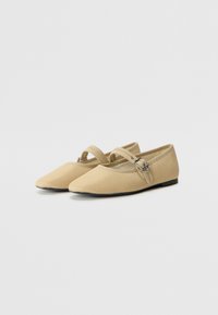 Bailarinas beige con un diseño de punta, hechas de tela suave. Cuentan con una correa para el tobillo con una hebilla de metal y una suela plana.