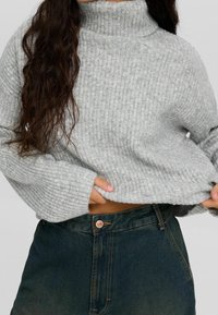 Pull à col roulé côtelé gris avec manches longues, doté d'une coupe décontractée et de poignets retroussés, associé à un jean en denim foncé taille haute.