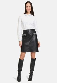 Gonna di pelle nera con due tasche con zip, abbinata a una camicia bianca con bottoni dotata di colletto a punta e dettagli sul colletto.