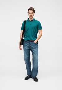 Γαλάζιο πόλο πουκάμισο με γιακά, συνδυασμένο με ανοιχτό μπλε τζιν παντελόνι με ίσια γραμμή. Μαύρα παπούτσια και μια μικρή τσάντα ώμου συμπληρώνουν την εμφάνιση.