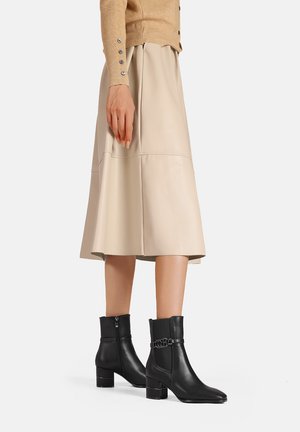 Stivali neri in pelle alla caviglia con punta quadrata, tacco corto a blocco e zip laterale. Abbinati a una gonna midi plissettata beige.