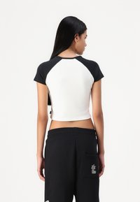 Black and white cropped T-shirt with short sleeves, featuring a round neckline and contrasting raglan sleeves. Smooth texture and minimal design.
