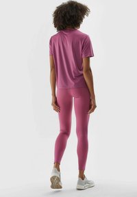 Rosa Sportoberteil und Leggings aus glattem Stoff, mit einer figurnahen Passform. Getragen mit hellen Sportschuhen.