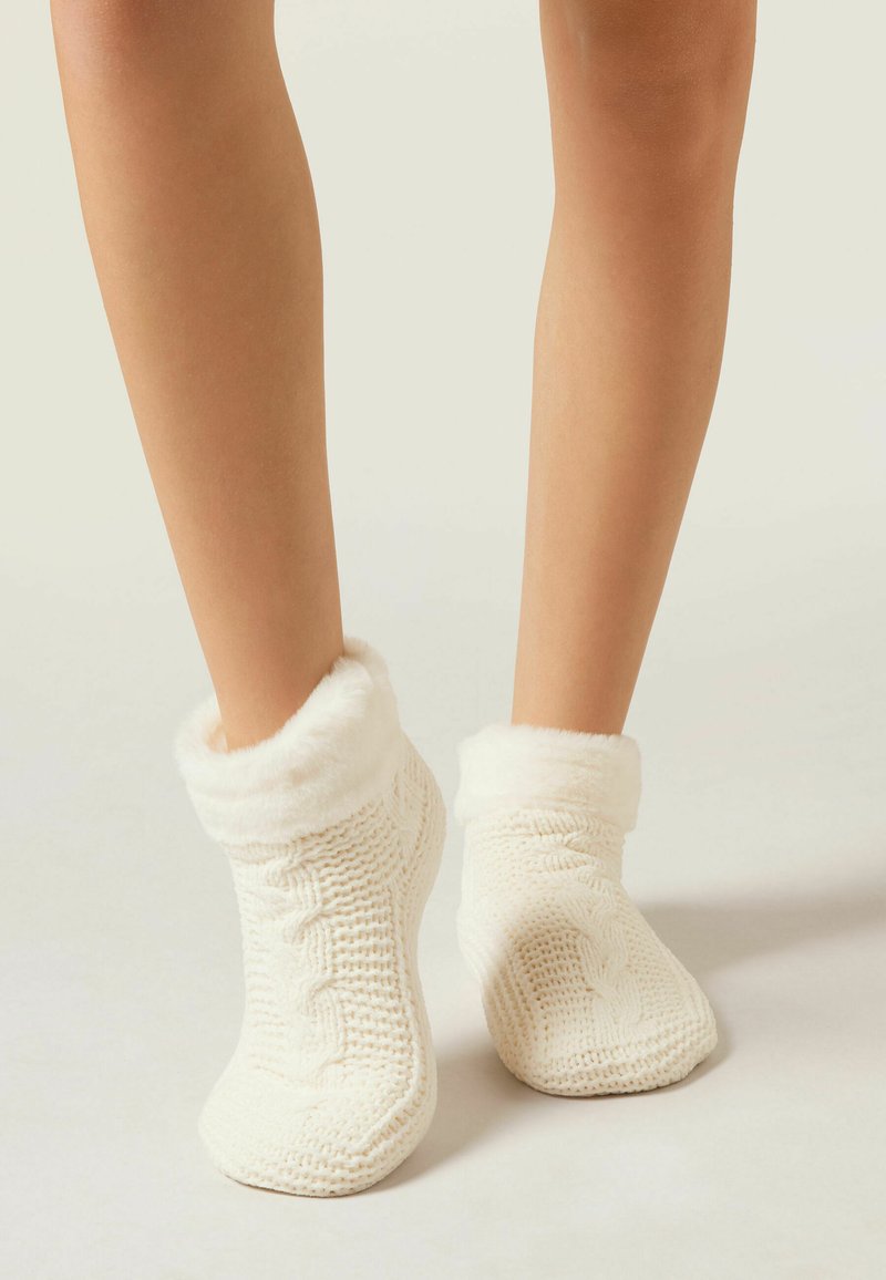 Jambes portant des chaussettes de cheville tricotées blanches avec un poignet doux et duveteux sur un fond clair.
