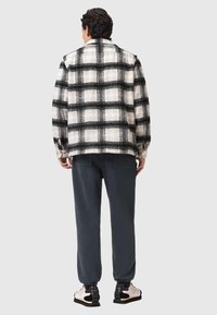 Marynarka w czarno-białą kratę o luźnym kroju; zestawiona z ciemnymi spodniami i jasnymi sneakersami z czarnymi akcentami.