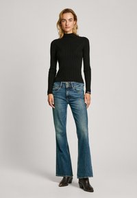 Svart ribbad polokrage tröja kombinerad med ljusblå vida jeans. Jeansen har en femfickdesign och bärs med svarta ankelstövlar.