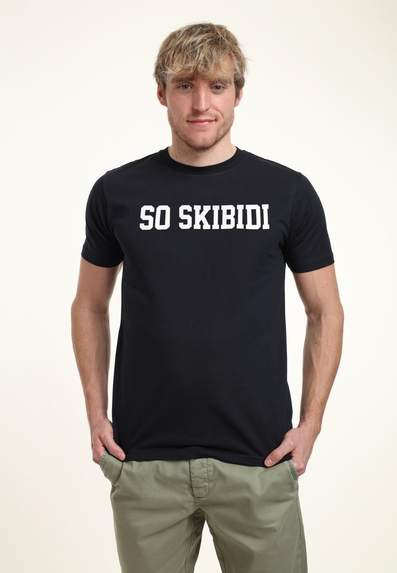 Černé bavlněné tričko s nápisem "SO SKIBIDI" v tučných bílých písmenech. Krátké rukávy a kulatý výstřih. Nosit s světlými zelenými kalhotami.