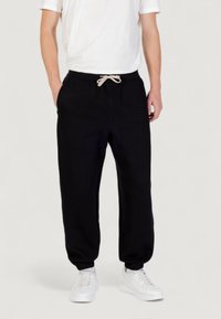 Zwarte sweatpants van een zachte stof met een elastische tailleband en een trekkoord. Aansluitende manchetten en zijzakken. Gecombineerd met witte sneakers.