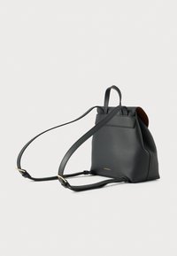 Mochila preta em pele com acabamento texturizado, formato afunilado, pega superior e alça ajustável. Logo minimalista dourado na lateral.