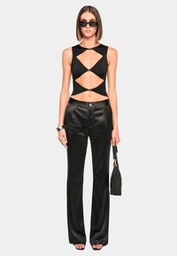 Black cutout bodysuit features a scoop neckline, midriff cutouts, and silver hardware accents. Paired with high-waisted black satin pants.