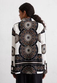 Camicia a maniche lunghe con un motivo geometrico in toni di nero, bianco e marrone, con una vestibilità comoda e una texture di tessuto morbido.