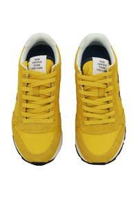 Sneakers atletici gialli con tomaia in tessuto testurizzato, punta tonda e dettagli neri a contrasto. I lacci sono gialli; la linguetta presenta testo stampato.