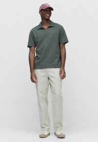 Kortärmad, texturerad grön polo med krage, ihop med ljusbeige byxor och beiga sneakers; vinröd keps med vit text.