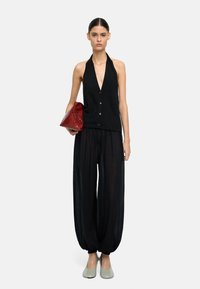 Czarny top na halter, z dekoltem w kształcie litery V, zapięty na guziki; przezroczyste czarne spodnie o szerokich nogawkach. Modelka trzyma czerwoną kopertówkę, ma na sobie jasnoszare obuwie.