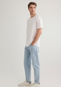 Helles rosa Baumwoll-T-Shirt mit Rundhalsausschnitt, kombiniert mit hellblauen Jeans und beigen Sneakers mit grünen und marineblauen Akzenten.