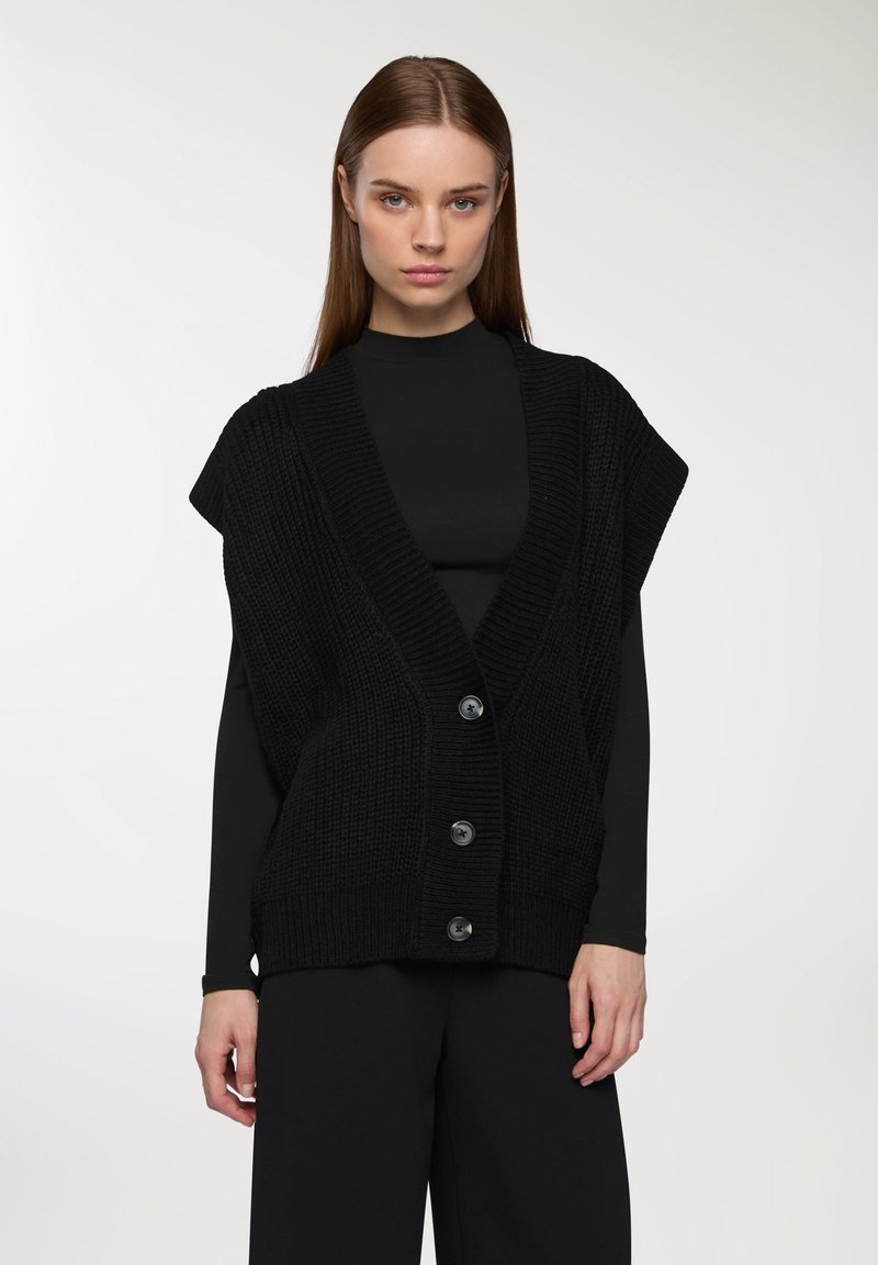 Cardigan senza maniche nero a maglia con scollo a V profondo e cinque bottoni. Presenta un tessuto testurizzato e una vestibilità comoda.