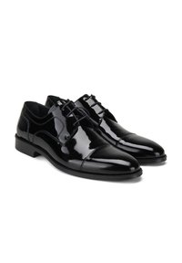 Chaussures habillées en cuir verni noir avec un bout rond, des lacets à l'avant, des détails de couture subtils et un petit talon empilé.