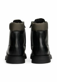 Ein Paar schwarze Lederstiefeletten mit gepolsterten grauen Kragen und robusten Gummisohlen, von hinten auf einem weißen Hintergrund betrachtet.