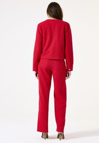 Pull en maille texturée rouge et pantalon assorti, design ajusté, forme droite, avec des boutons décoratifs aux manches et aux poches arrière.