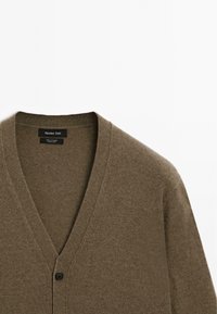 Cardigan in cashmere marrone con scollatura a V, chiusura con un singolo bottone nero e texture a coste. Etichetta visibile nella zona del colletto.