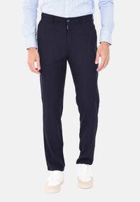 Pantaloni blu navy realizzati in tessuto morbido, con chiusura a bottone, taglio dritto e tasche frontali. Indossati con sneaker bianche.