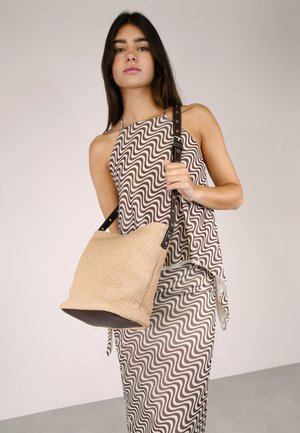 Bolso de mano tejido en tono marrón claro con una correa resistente de color marrón, que presenta un cuerpo suave y texturizado y una base estructurada. El patrón es abstracto, ondulado y marrón.